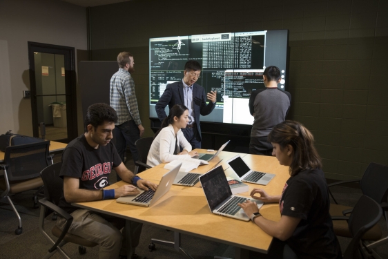 photo of six people in a room with laptop and projection screen, table